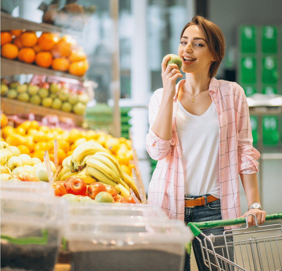 A woman is about to take a bite of a fruit in the market.