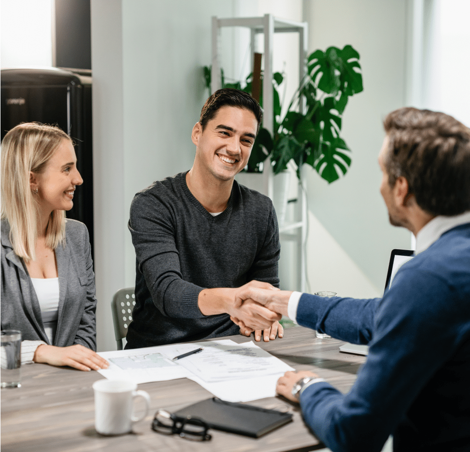 An office worker shakes hands with a man while he is in the company of a woman.